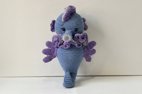 A handcrafted blue crochet seahorse with purple accents and a crochet pattern.